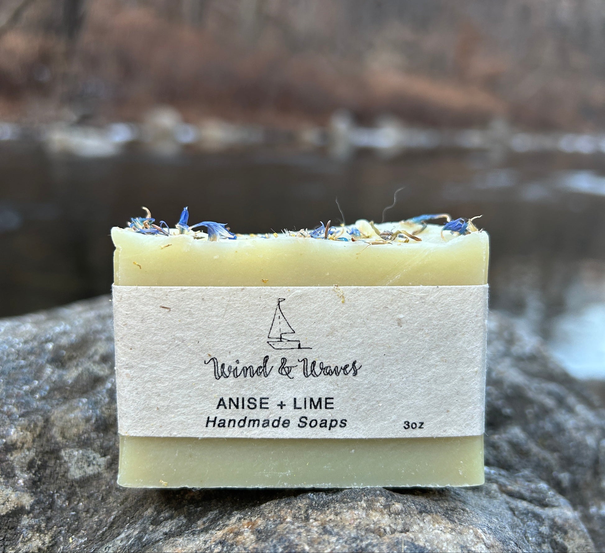 Handmade anise and lime soap bar, enriched with organic coconut oil, olive oil, shea butter, mango seed butter, and cocoa butter. Features natural colorants like spinach powder and French green clay, with cornflower petals for a decorative touch. Scented with anise, lime, and peppermint essential oils. Each bar weighs approximately 3 ounces and is wrapped in eco-friendly lokta paper.